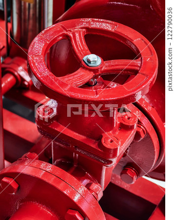 Detailed close-up of a red valve on industrial piping system showcasing mechanical precision and vibrant color 122790036