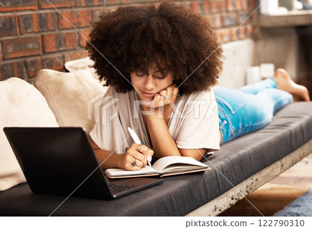 Education, learning and writing with a woman student studying online with her laptop on a sofa in her home living room. Study, growth and development with a female learner taking notes for an exam 122790310