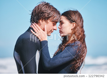 Young surfing couple hug, share intimate moment on beach vacation, flirting and playful. Girlfriend and boyfriend embracing, enjoying their romance and relationship while being free together outside 122790342