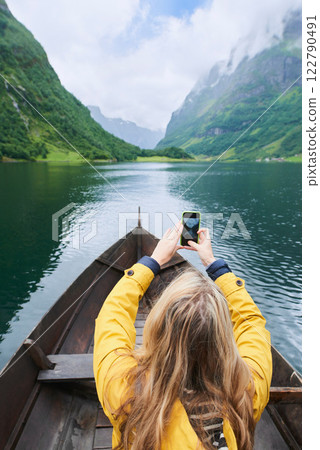 Adventure woman in row boat taking photo on smart phone of beautiful fjord lake for social media Adventure woman in row boat taking photo on smart phone of beautiful fjord lake for social media 122790491