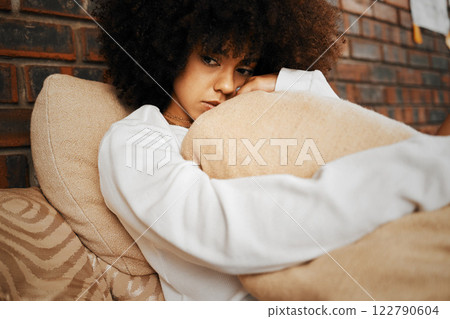 Sad, depressed and lonely black woman with mental health problems hugging a pillow at home. Portrait of a African afro female in depression, stress and anxiety feeling unhappy living alone in a house 122790604