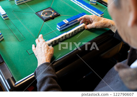 The hands of a senior man playing mahjong on an electric mahjong table 122790607