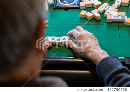 The hands of a senior man playing mahjong on an electric mahjong table 122790708
