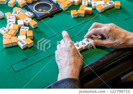 The hands of a senior man playing mahjong on an electric mahjong table 122790710
