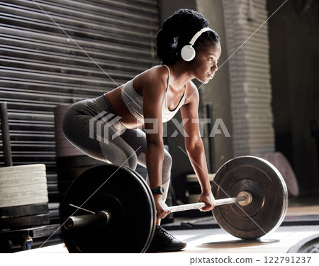 Power, fitness and headphones of a woman with barbell weight lift exercise, workout or training in wellness gym. Sports black woman listening to motivation music for muscle, strength and health 122791237