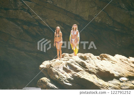Summer, bikini and holiday, women on a cliff in the sun, ready to jump into the water. Travel, beauty and adventure, young girls relax on vacation in the sun with rock face or cave in the background. Summer, bikini and holiday, women on a cliff in the sun, ready to jump into the water. Travel, beauty and adventure, young girls relax on vacation in the sun with rock face or cave in the background. 122791252