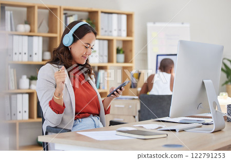 Employee, on phone and headphones in office listening to music while browsing social media. Happy and excited business woman with smile receives good news on her mobile device in corporate building 122791253