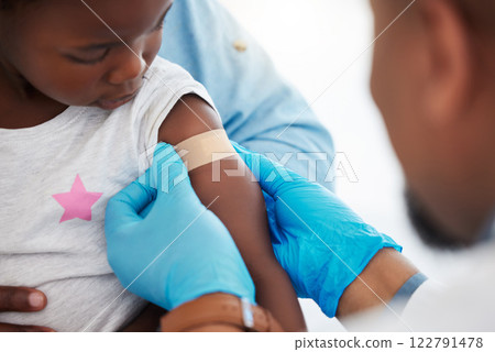 Doctor, healthcare worker and medical professional with plaster on arm of sick child after covid vaccine, doing checkup after injury and protect from virus. African girl at clinic consultation 122791478