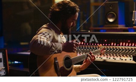 Young artist songwriter composing a new song on guitar in recording session at studio, creating tunes and editing them after in post production. Musician composer producing tracks. Camera A. 122791725