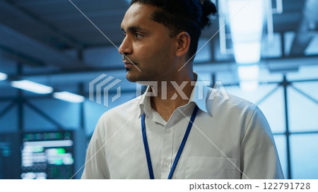 System administrator walks in data center used for managing gear energy consumption, working on tablet. Close up of IT specialist using device in workspace used for automation in server room, camera A 122791728