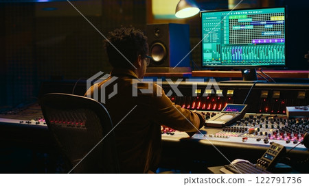 African american audio engineer uses compressor and mixer in professional studio, changing volume level and sound settings on a recording. Music production in control room. Camera A. African american audio engineer uses compressor and mixer in professional studio, changing volume level and sound settings on a recording. Music production in control room. Camera A. 122791736