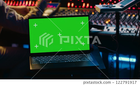 Music production engineer mixing and mastering music in control room, using laptop with greenscreen display. Skilled audio technician working with recording software on pc, pushing faders. Camera A. 122791917