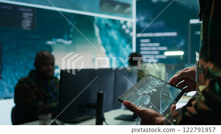 Military officer leads cybersecurity operations in a high tech operation room command post, ensuring data protection. Soldiers working with cctv surveillance systems, satellite imagery. Camera B. 122791957