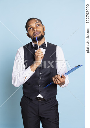 Hotel worker writing down notes on clipboard files against blue background, ensuring easy check in process for guests. Bellboy providing excellent concierge services, hospitality industry. Hotel worker writing down notes on clipboard files against blue background, ensuring easy check in process for guests. Bellboy providing excellent concierge services, hospitality industry. 122792090