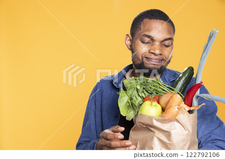 Young adult feels confident with his paper bag full of bio groceries, preparing to cook something vegan. African american guy satisfied with his zero waste way of living, healthy eating. Young adult feels confident with his paper bag full of bio groceries, preparing to cook something vegan. African american guy satisfied with his zero waste way of living, healthy eating. 122792106