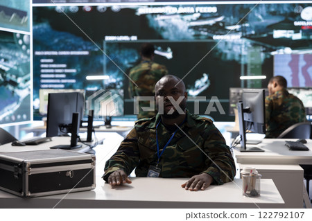 Military intelligence expert conducts a strategic teleconference connection in a modern command post, utilizing real time data on multiple screens for effective communication and decision making. Military intelligence expert conducts a strategic teleconference connection in a modern command post, utilizing real time data on multiple screens for effective communication and decision making. 122792107
