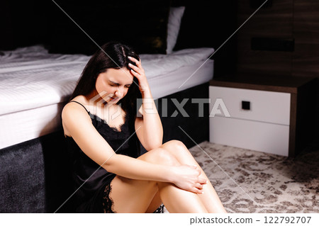 Unhappy woman touching hair, sitting on floor at home, thinking about problems. Upset girl feeling lonely and sad, psychological and mental troubles, suffering from bad relationship or break up 122792707