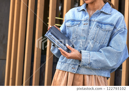 Fashionable woman in denim jacket holding elegant wallet, stylish accessory focus, contemporary fashion concept Fashionable woman in denim jacket holding elegant wallet, stylish accessory focus, contemporary fashion concept 122793102