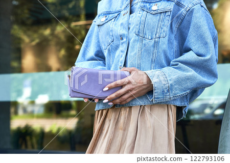 Stylish woman in denim jacket holding fashionable purple purse, close-up on trendy street fashion, accessory concept 122793106