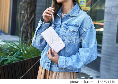 Woman wearing denim jacket, holding leather purse, casually posed, outdoor setting, fashion accessory, city lifestyle concept Woman wearing denim jacket, holding leather purse, casually posed, outdoor setting, fashion accessory, city lifestyle concept 122793110