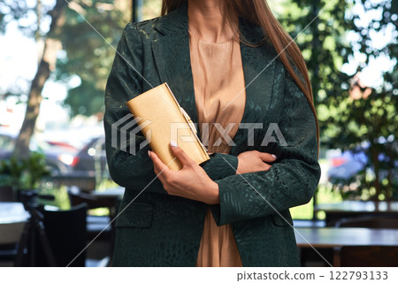 Elegant woman, gold clutch, green jacket, outdoor setting, refined fashion look, sophisticated style, secured wallet, day elegance, fashion focus concept 122793133