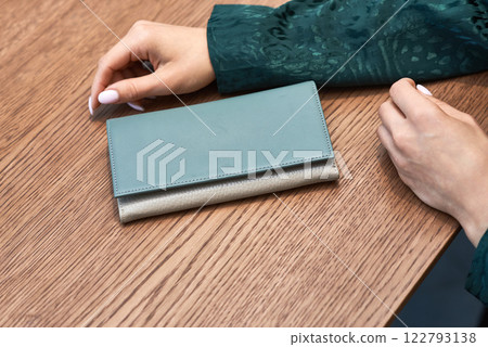 Elegant leather wallet placed on wooden table, paired with stylish woman's hands, showcasing modern fashion accessory concept 122793138