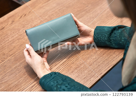 Woman holding elegant green wallet with sleek design against wooden table background fashion accessory concept 122793139