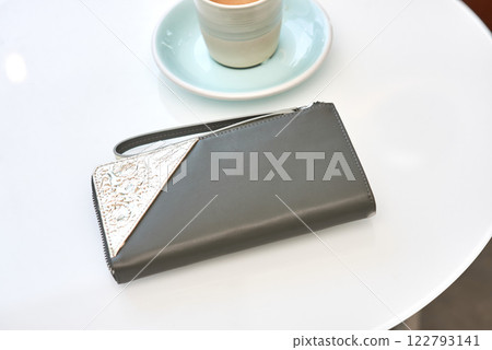 Elegant leather wallet with embossed texture next to coffee cup on white surface, minimal lifestyle concept 122793141