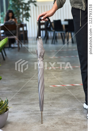 Person holding elegant closed umbrella indoors near plants with stylish seating area concept Person holding elegant closed umbrella indoors near plants with stylish seating area concept 122793158