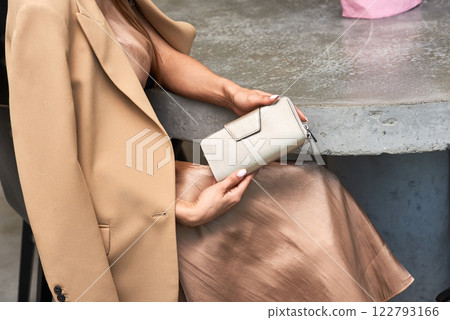 Elegant woman holding stylish beige wallet sitting in cafe dressed in fashionable outfit, luxury accessory concept 122793166