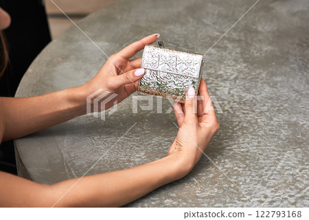 Elegant hands holding ornate silver wallet on stone table, showcasing intricate design and craftsmanship, luxury accessory concept. 122793168