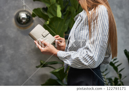 Elegant woman in striped blouse holding stylish leather wallet in indoor greenery setting, sophisticated fashion concept 122793171
