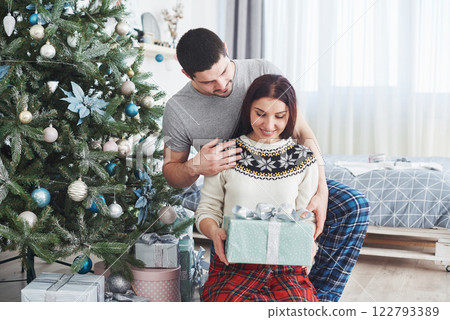 Young couple celebrating Christmas. A man suddenly presented a present to his wife. The concept of family happiness and well-being Young couple celebrating Christmas. A man suddenly presented a present to his wife. The concept of family happiness and well-being 122793389