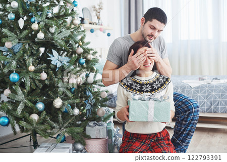 Young couple celebrating Christmas. A man suddenly presented a present to his wife. The concept of family happiness and well-being Young couple celebrating Christmas. A man suddenly presented a present to his wife. The concept of family happiness and well-being 122793391