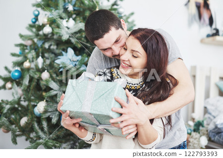 Young couple celebrating Christmas. A man suddenly presented a present to his wife. The concept of family happiness and well-being Young couple celebrating Christmas. A man suddenly presented a present to his wife. The concept of family happiness and well-being 122793393
