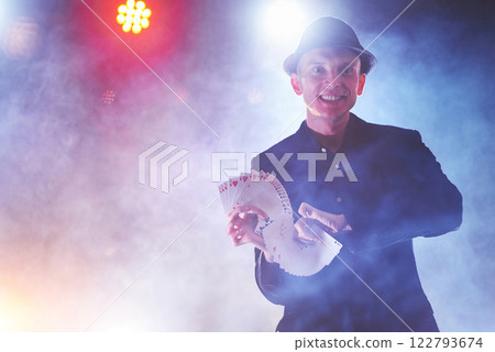 Magician showing trick with playing cards. Magic or dexterity, circus, gambling. Prestidigitator in dark room with fog Magician showing trick with playing cards. Magic or dexterity, circus, gambling. Prestidigitator in dark room with fog 122793674