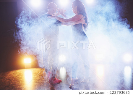 Skillful dancers performing in the dark room under the concert light and smoke. Sensual couple performing an artistic and emotional contemporary dance Skillful dancers performing in the dark room under the concert light and smoke. Sensual couple performing an artistic and emotional contemporary dance 122793685