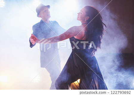 Skillful dancers performing in the dark room under the concert light and smoke. Sensual couple performing an artistic and emotional contemporary dance Skillful dancers performing in the dark room under the concert light and smoke. Sensual couple performing an artistic and emotional contemporary dance 122793692