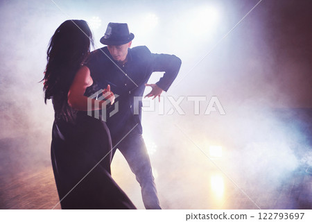 Skillful dancers performing in the dark room under the concert light and smoke. Sensual couple performing an artistic and emotional contemporary dance Skillful dancers performing in the dark room under the concert light and smoke. Sensual couple performing an artistic and emotional contemporary dance 122793697