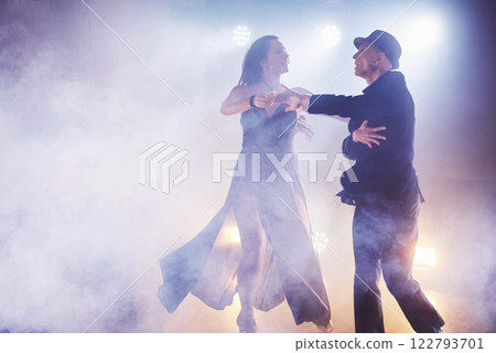 Skillful dancers performing in the dark room under the concert light and smoke. Sensual couple performing an artistic and emotional contemporary dance Skillful dancers performing in the dark room under the concert light and smoke. Sensual couple performing an artistic and emotional contemporary dance 122793701