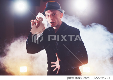 Magician showing trick with playing cards. Magic or dexterity, circus, gambling. Prestidigitator in dark room with fog Magician showing trick with playing cards. Magic or dexterity, circus, gambling. Prestidigitator in dark room with fog 122793724