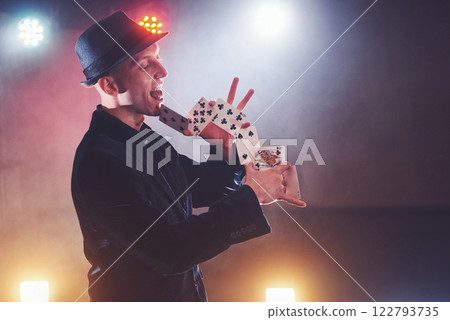 Magician showing trick with playing cards. Magic or dexterity, circus, gambling. Prestidigitator in dark room with fog Magician showing trick with playing cards. Magic or dexterity, circus, gambling. Prestidigitator in dark room with fog 122793735