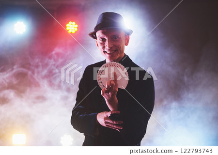 Magician showing trick with playing cards. Magic or dexterity, circus, gambling. Prestidigitator in dark room with fog 122793743