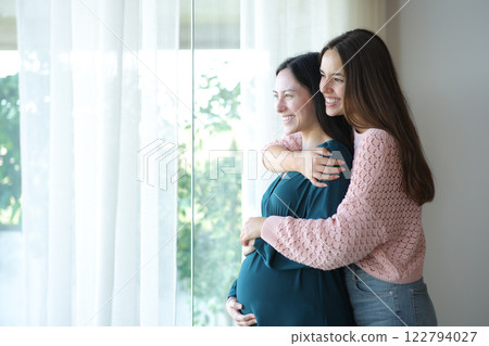 Happy lesbian pregnant asian woman and wife looking through a window 122794027
