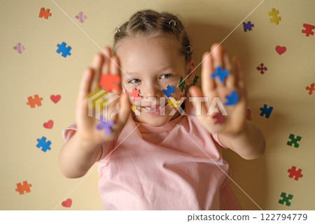 A child on a yellow studio background decorated with small pieces of multicolored puzzles. The girl shows her palms with the autism symbol. Intellectual development and education A child on a yellow studio background decorated with small pieces of multicolored puzzles. The girl shows her palms with the autism symbol. Intellectual development and education 122794779