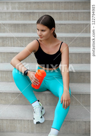beautiful woman sitting on  stairs relaxing before running outdoors holding a water bottle 122794985