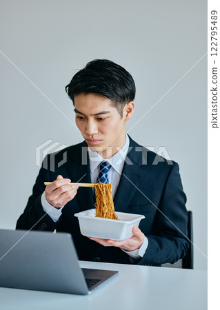 一名 20 多歲的年輕男子邊工作邊吃泡麵 122795489