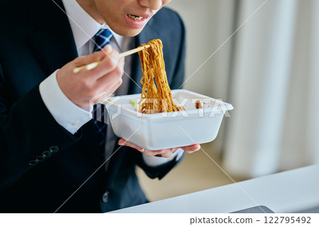 A young man in his 20s eating cup noodles while working A young man in his 20s eating cup noodles while working 122795492