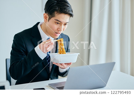 A young man in his 20s eating cup noodles while working 122795493