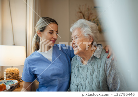 Caring healthcare worker visiting a senior patient at home, hugging her. 122796446